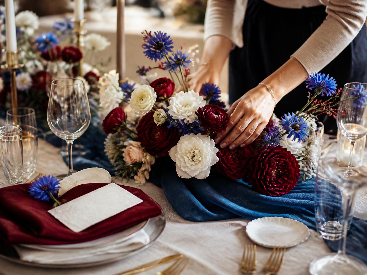 Décoratrice ajustant une composition florale dans un décor de table bleu et rouge